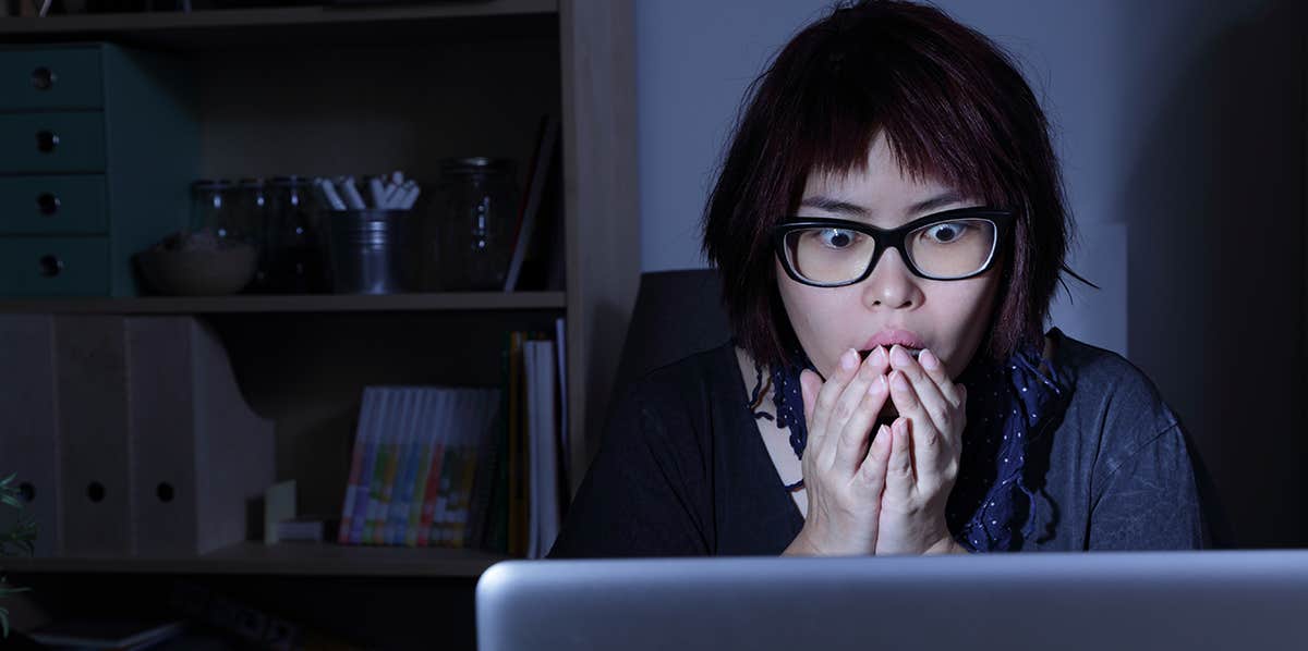 woman staring at computer screen at night, shocked