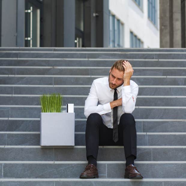 Man sitting on the steps with a box of his things after losing his job.
