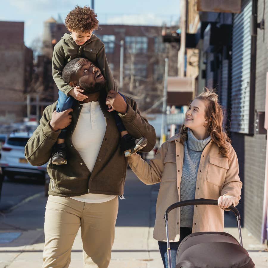 father holding toddler on shoulders and mother walking with baby in stroller