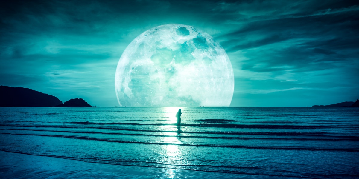 woman standing in front of a moon by water