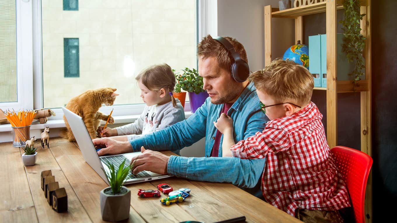 Man works on laptop with children playing around.