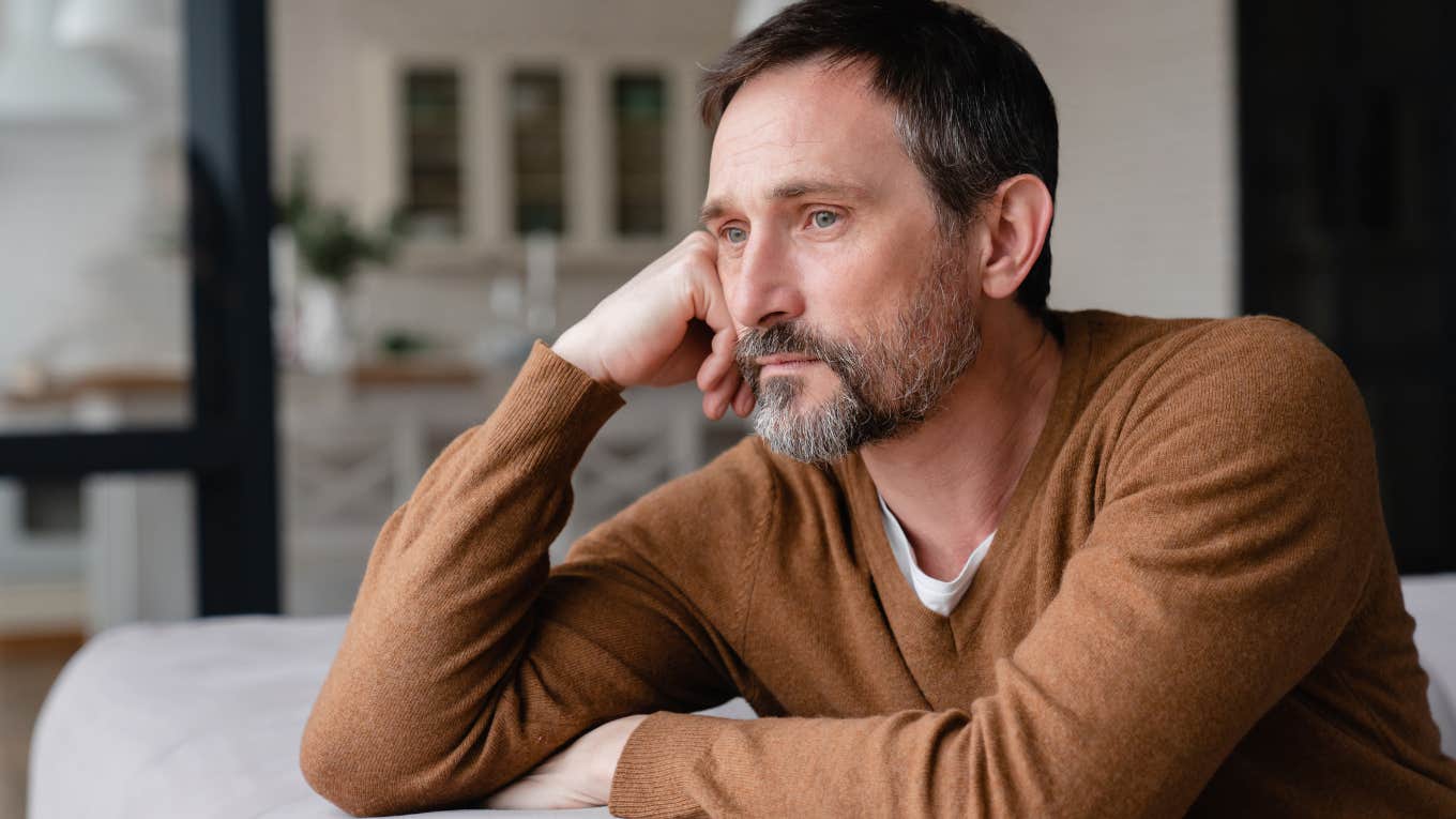 depressed man with hand on head looking out window