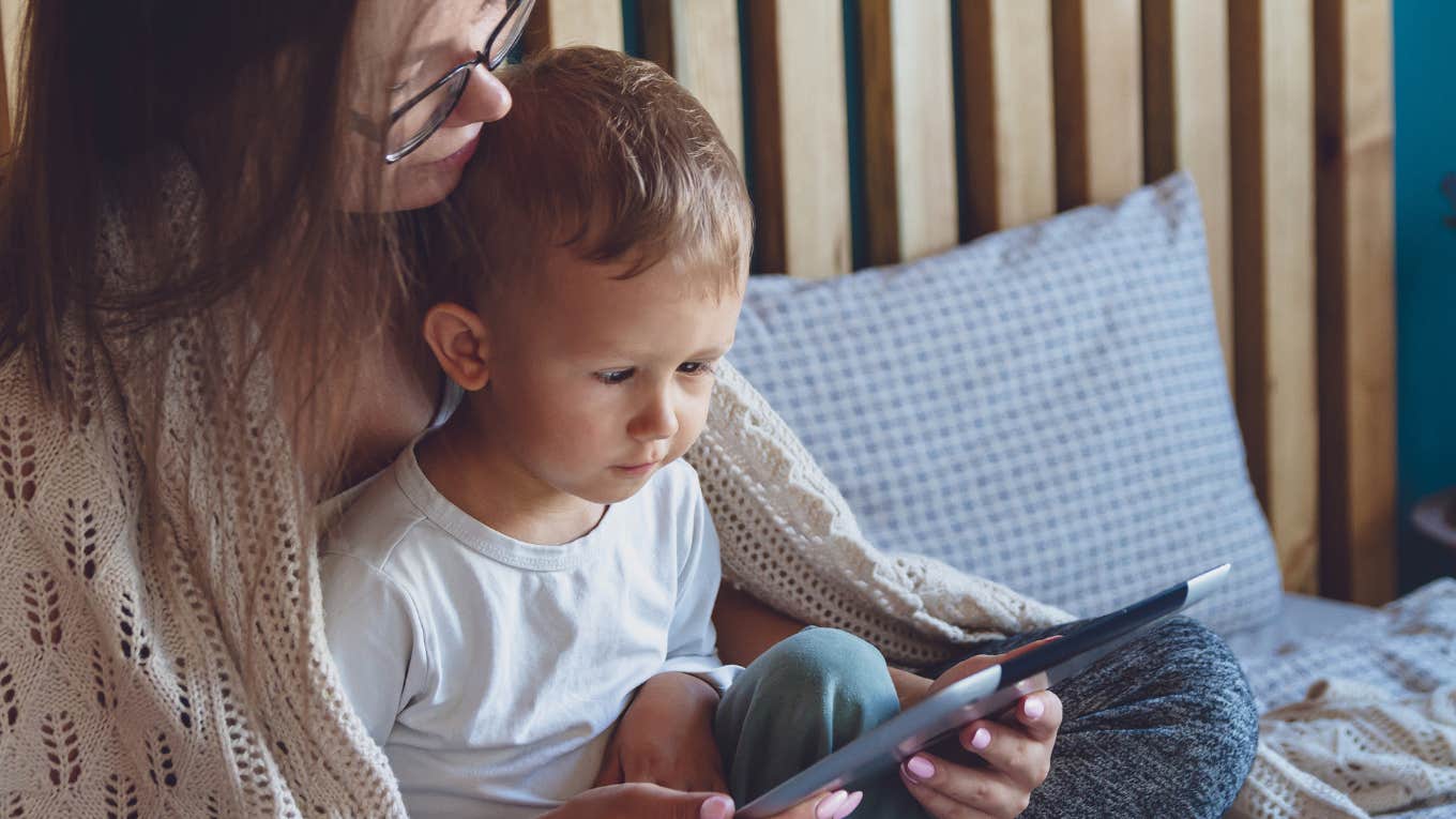 mom holding son while he plays on a tablet