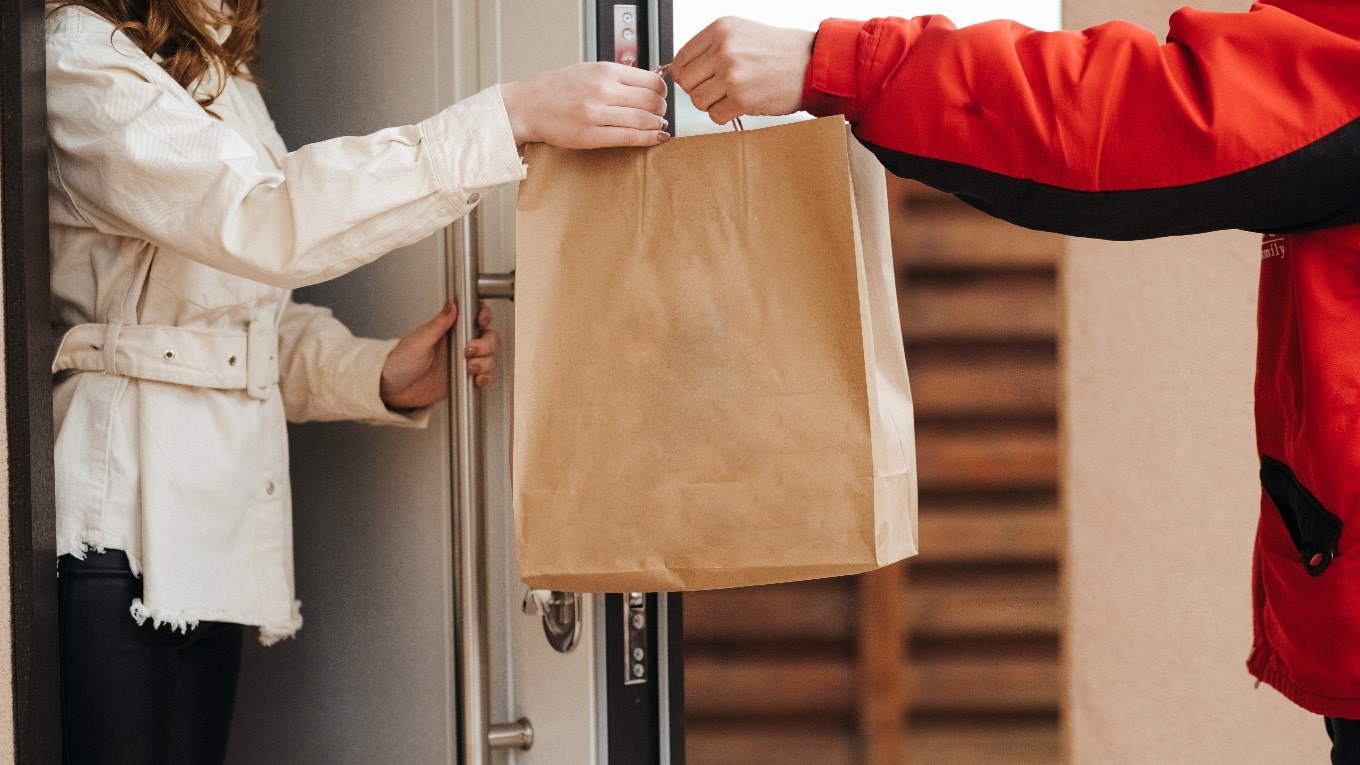 A food delivery driver is handing food to a woman.