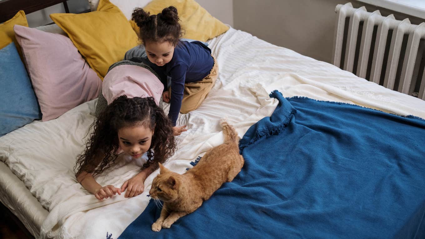 two young girls playing with a cat on a bed 