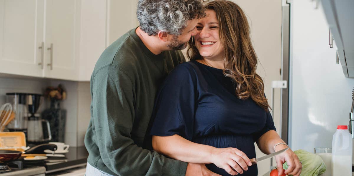husband embracing pregnant wife while standing in the kitchen