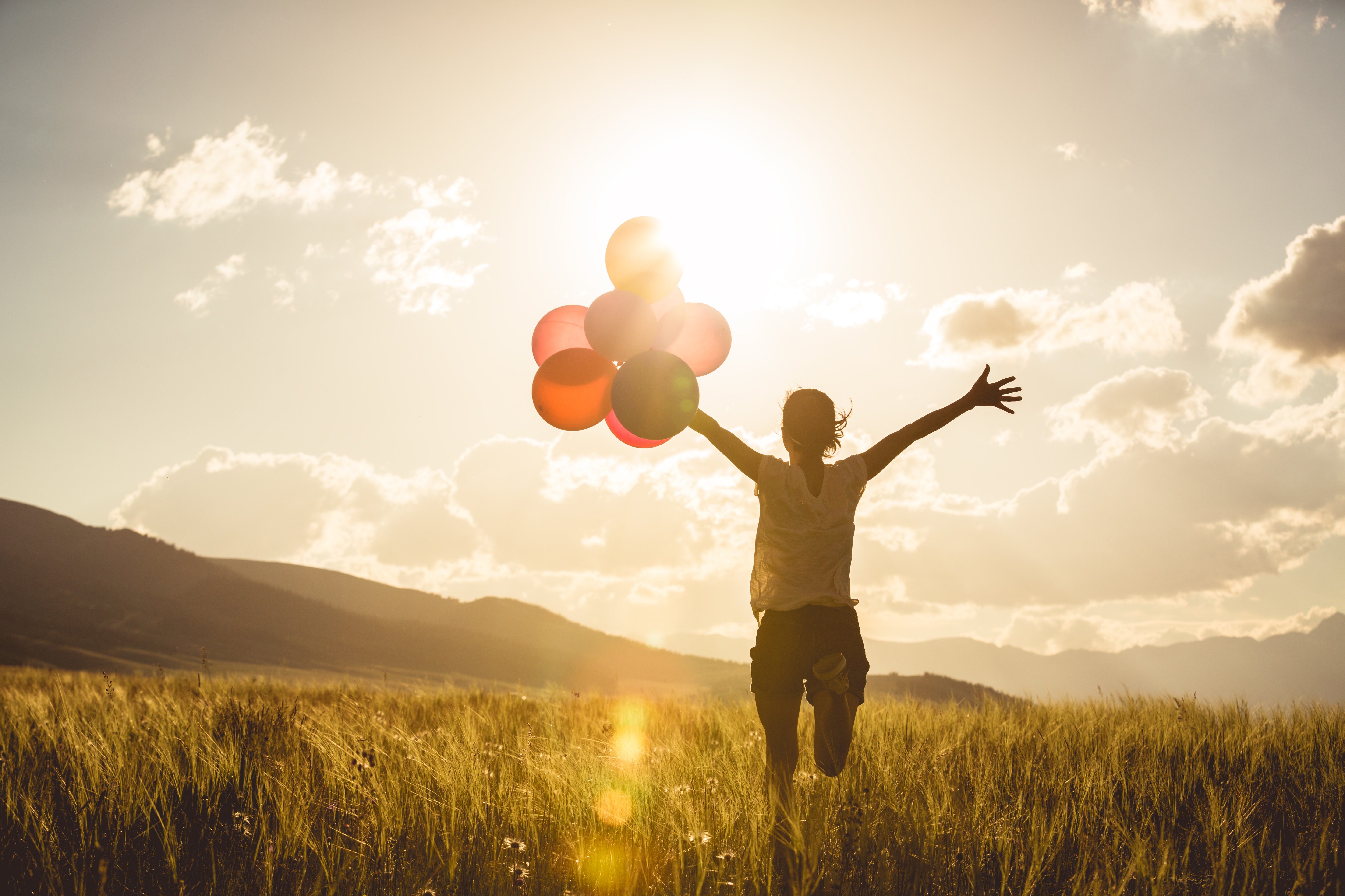 hopeful woman holding balloons while watching the sun
