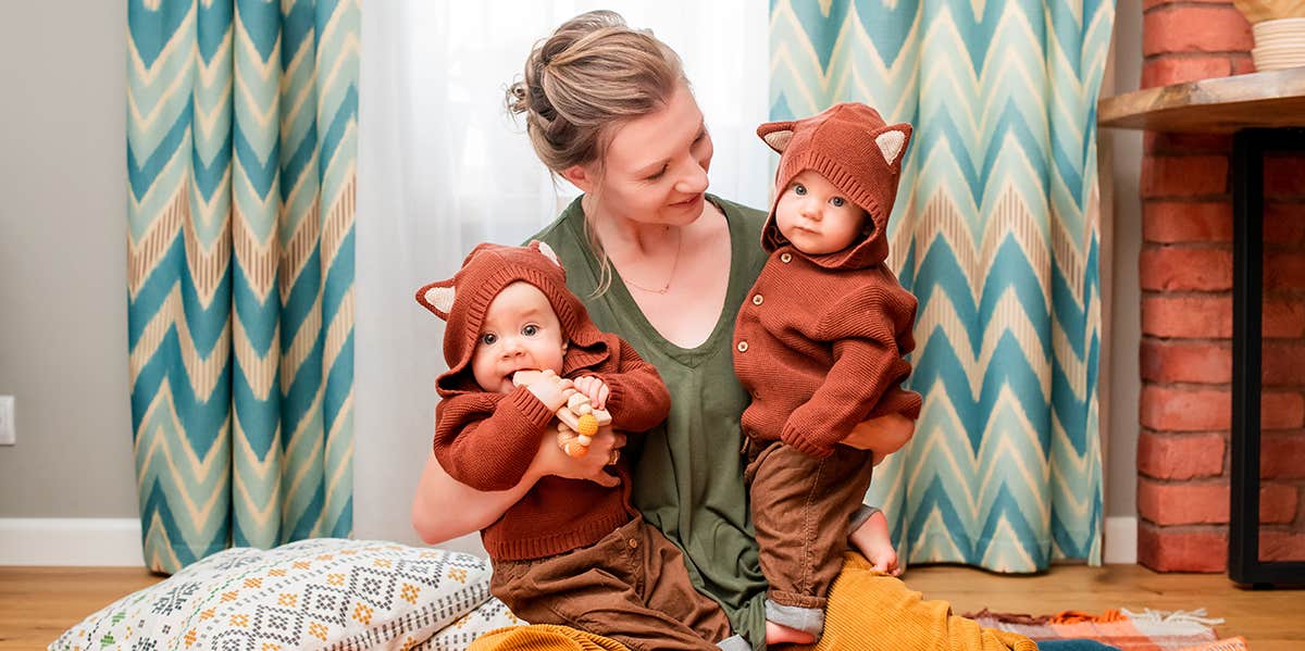 A photograph of a white woman holding two twins in identical animal outfits.