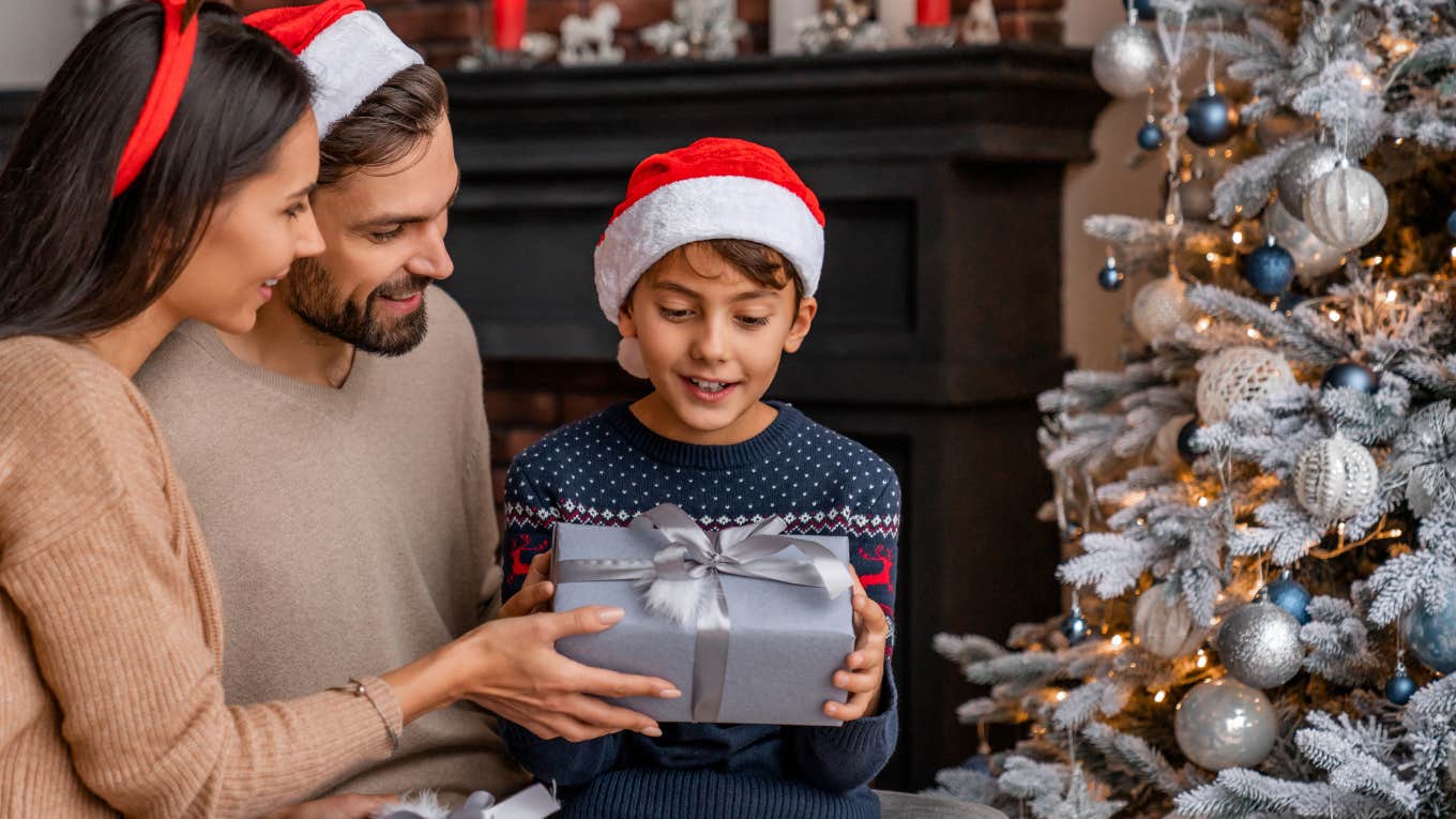 Parents giving present their son while sitting near Christmas tree in living room. 