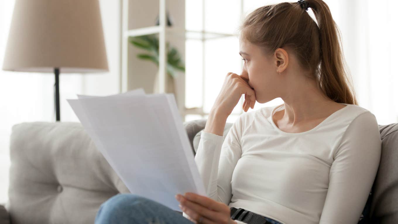 Woman reading baby book papers and looking upset. 