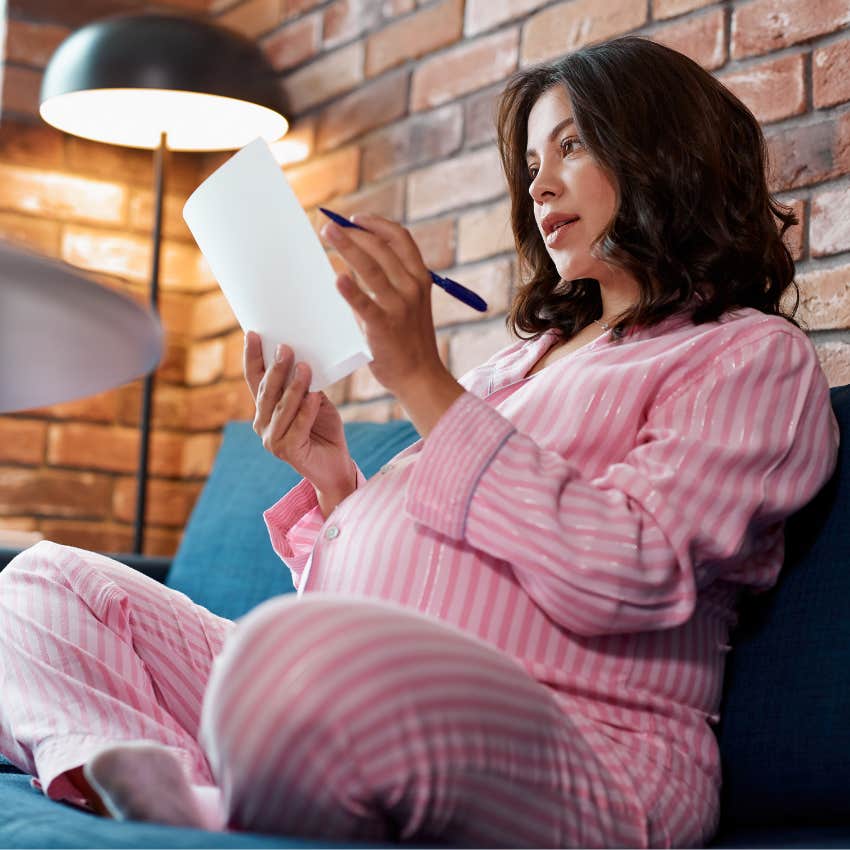 Pregnant woman writing on baby book pages. 