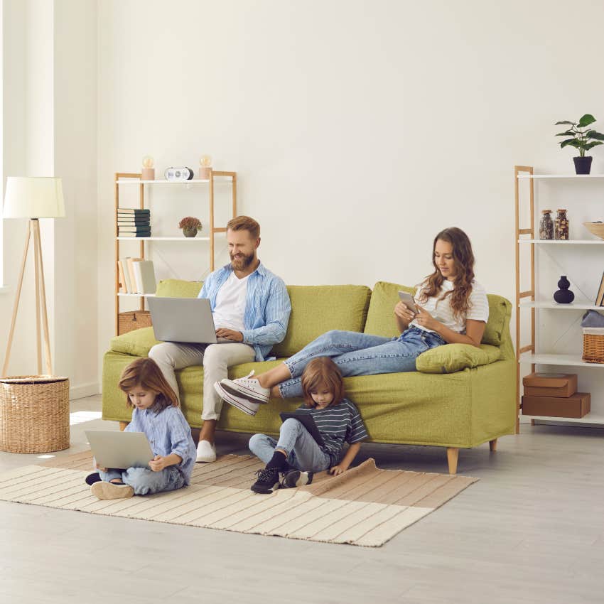 family sitting in living room while on tablets and laptops