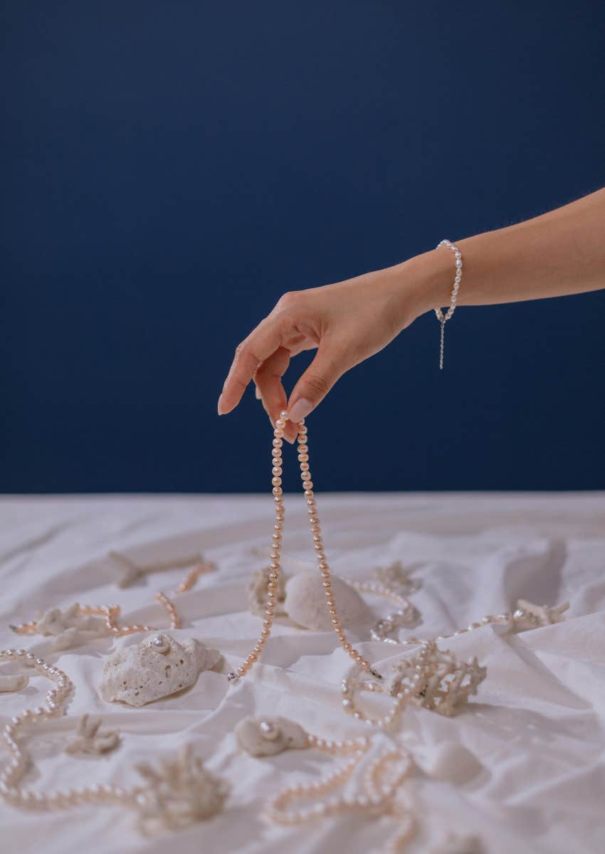 woman holding pearl jewelry over sand backdrop
