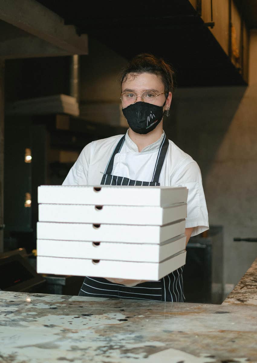 fast food worker holding boxes of pizza