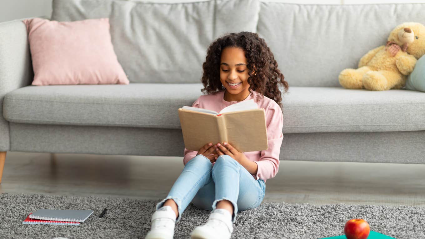 little girl sitting on the ground in front of a couch reading a book