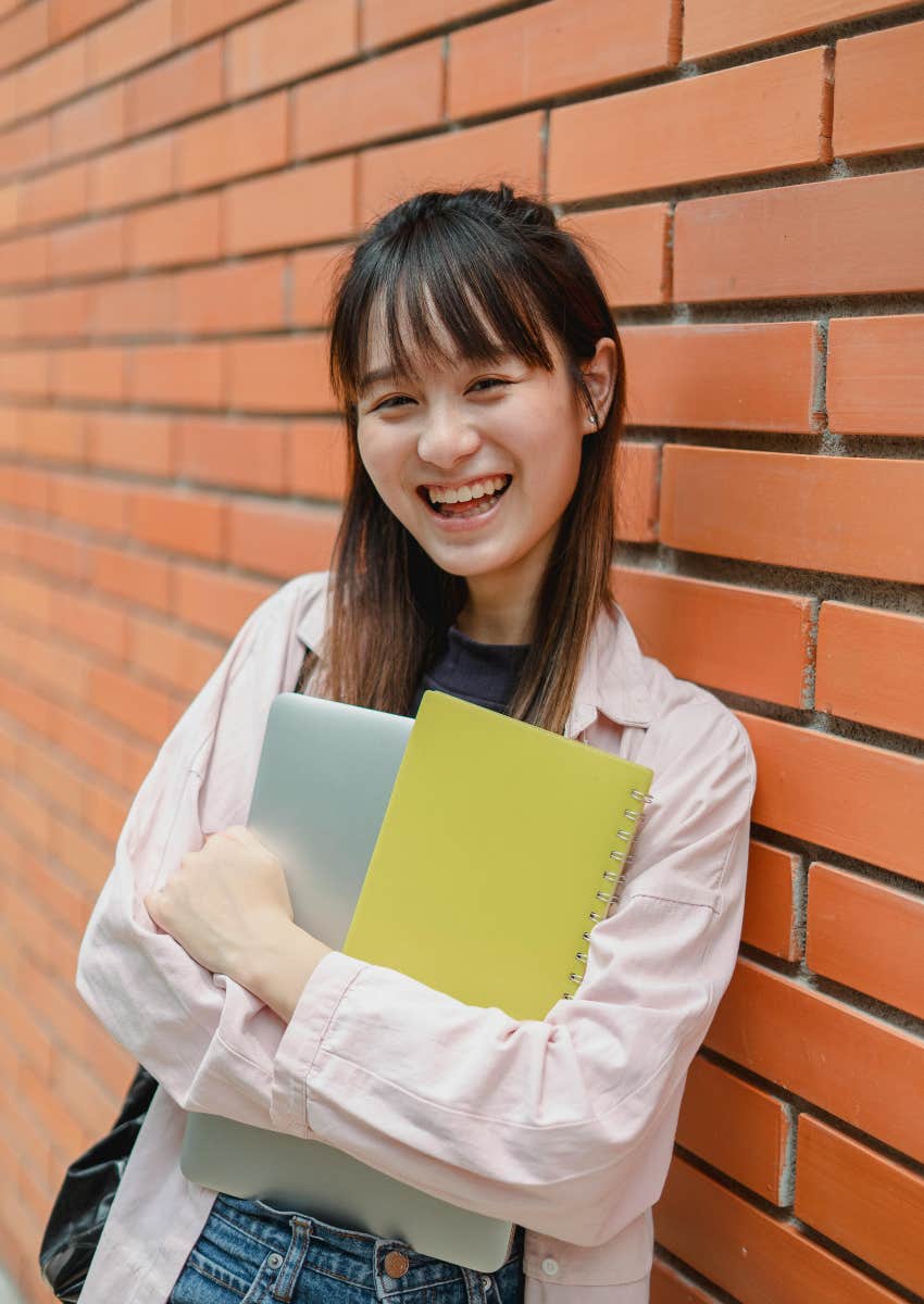 smiling female student holding notebook and laptop