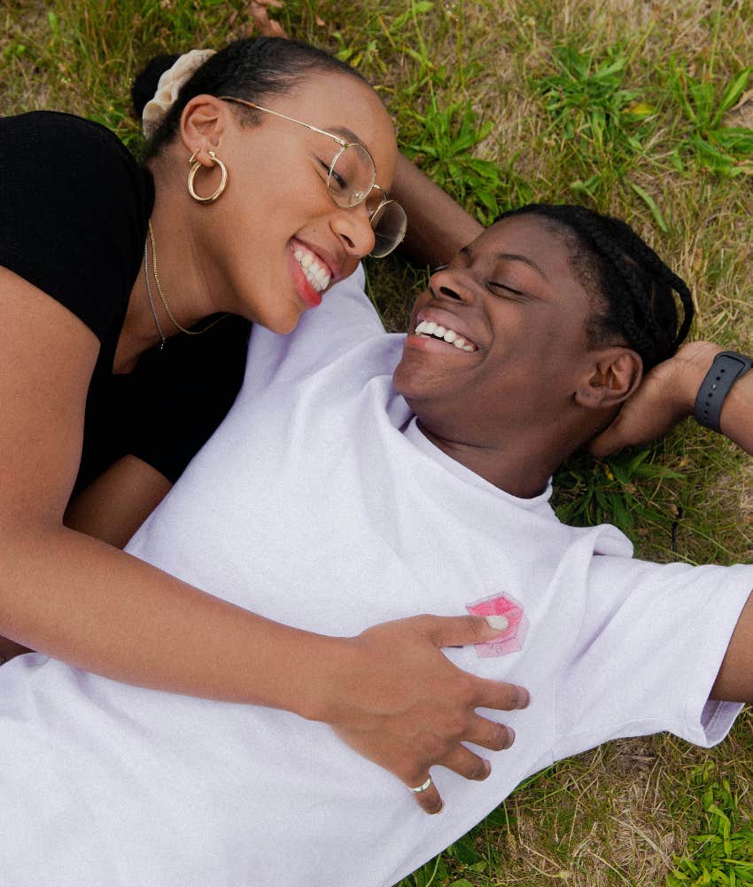 a couple smiling while lying the grass 
