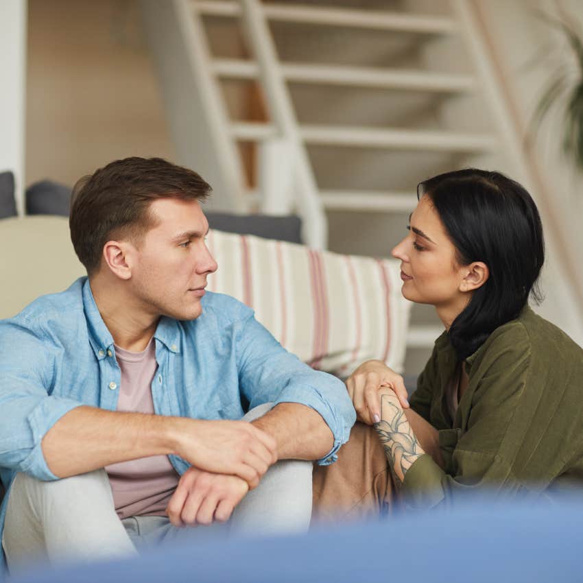  young couple talking to each other sincerely while sitting on floor in cozy home interior