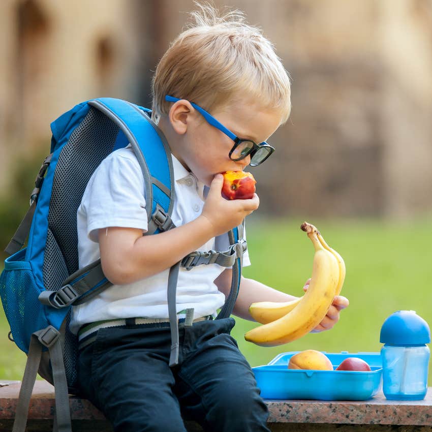 Little kid eating a school lunch outside. 