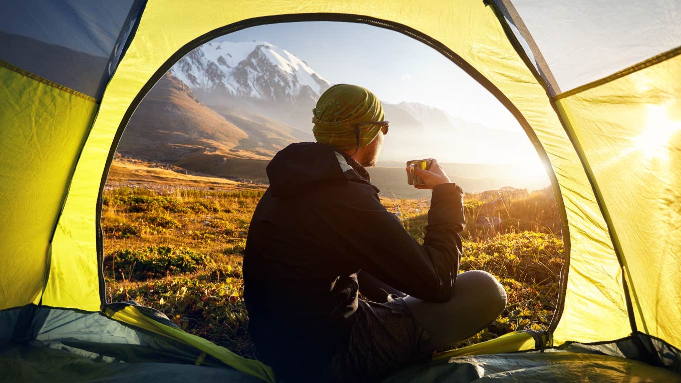 man sitting in the opening of a tent watching the sunrise