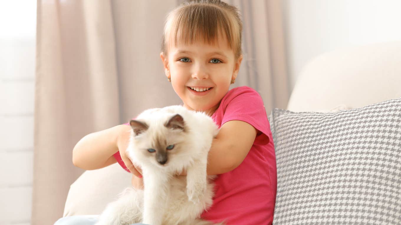 Little girl holding a cat and smiling. 