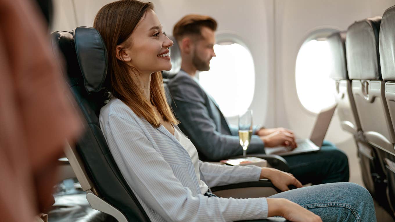 Cheerful woman sitting in seat in airplane next to man on laptop