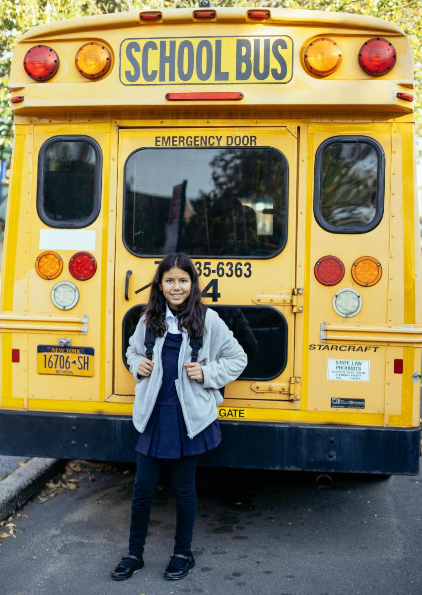 little girl standing at rear of school bus