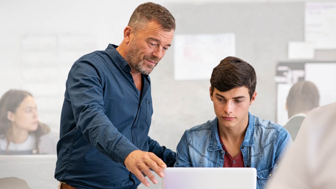 High school teacher talking to a student at laptop. 