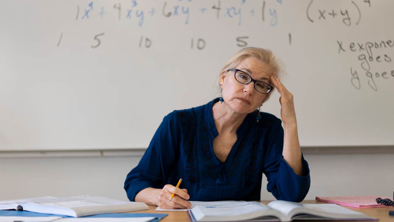 frustrated teacher sitting at desk in front of white board