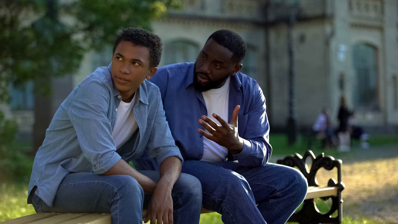 Black teenager ignoring scolding dad sitting on campus bench