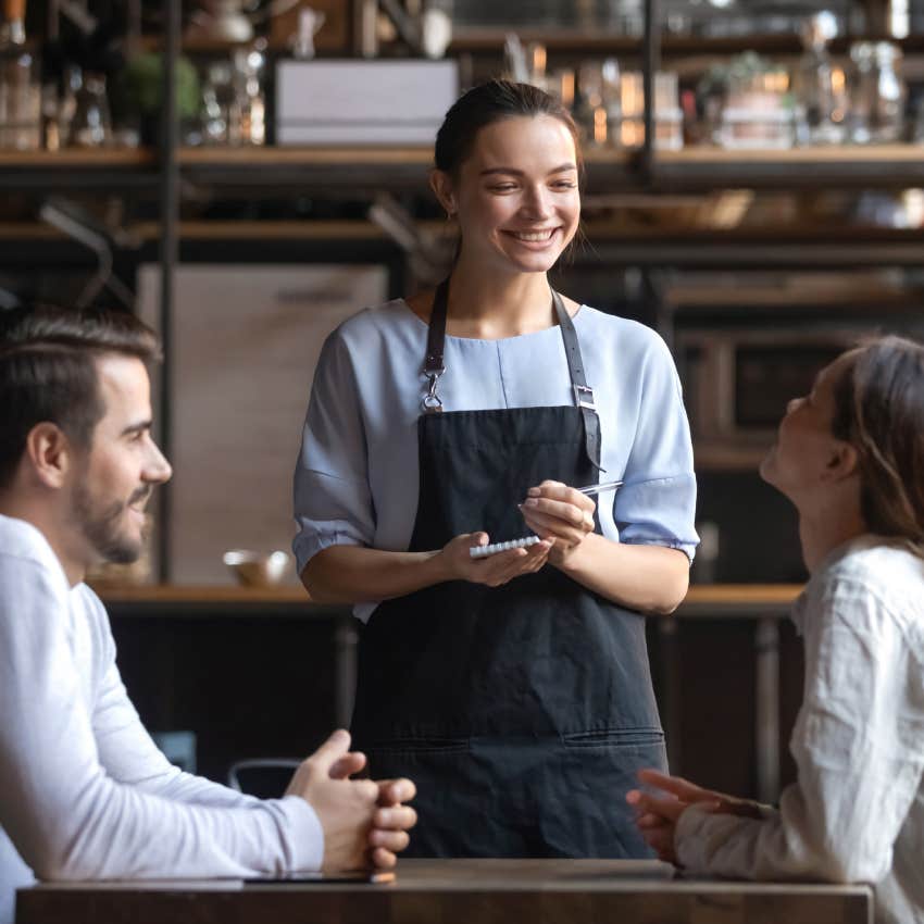 smiling waitress holding notepad to take order of couple at restaurant