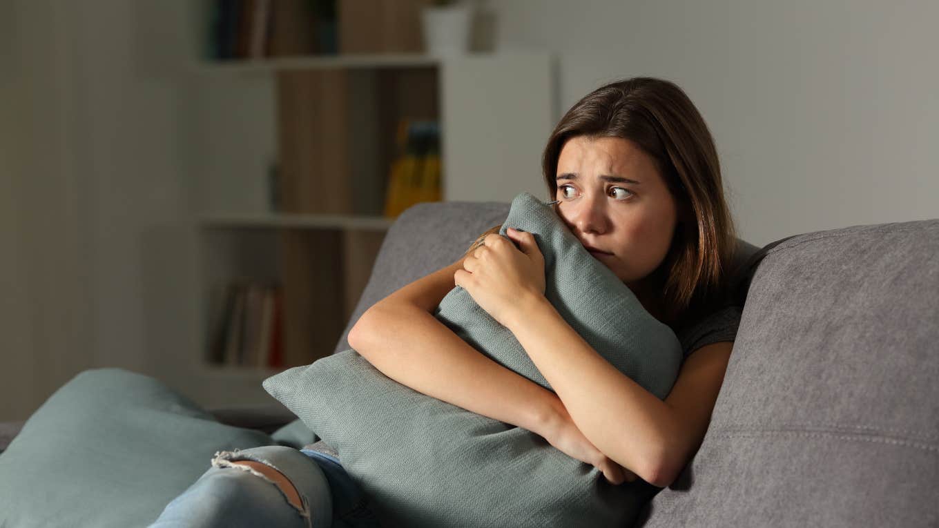 Scared woman at home embracing pillow sitting on a couch in the living room at home