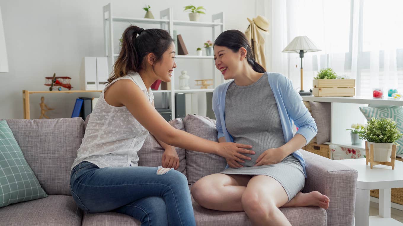 friend touching pregnant woman belly at baby shower party