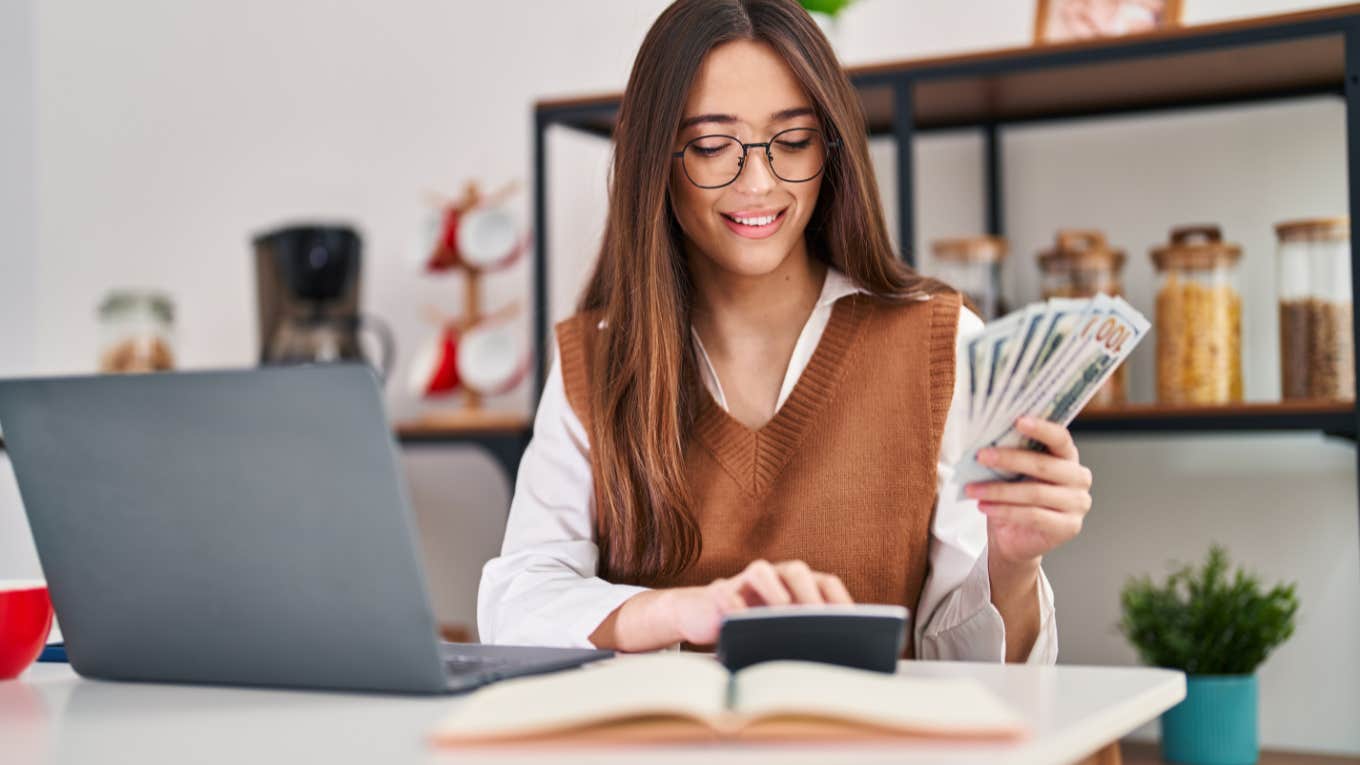  woman using laptop counting money at home