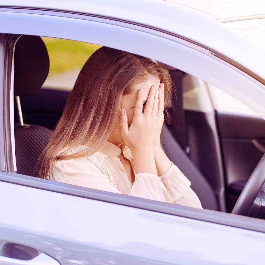 woman sitting in car with hands covering her face