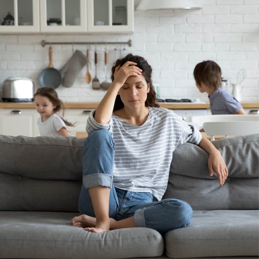 stressed woman sitting on couch as her kids run around
