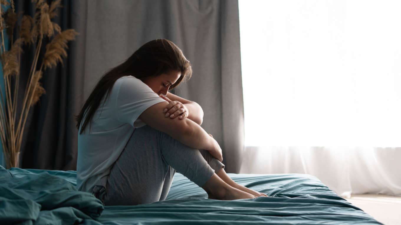 sad woman sitting on bed in bedroom with light from window