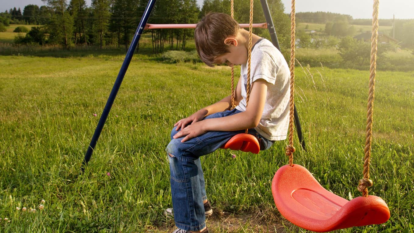 sad little boy alone on swing set