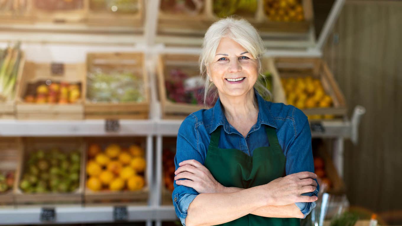 elderly grocery store employee standing in front of produce