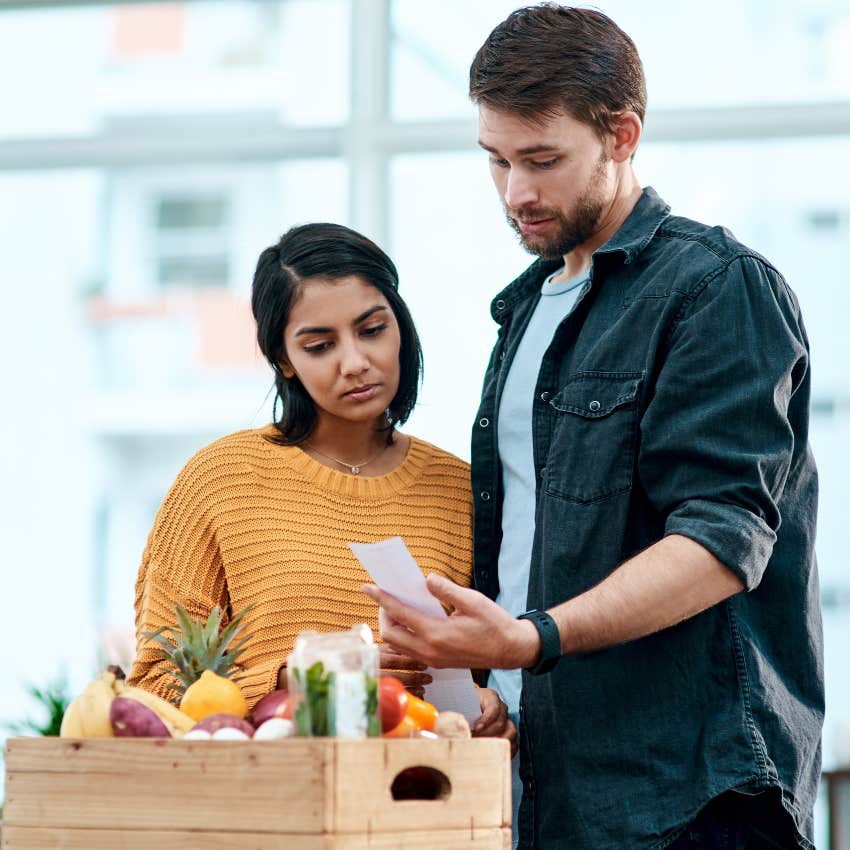 Couple looking concerned looking at grocery store receipt. 