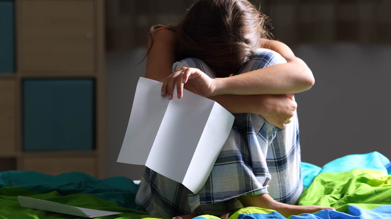 teen girl sitting on bed crying holding letter