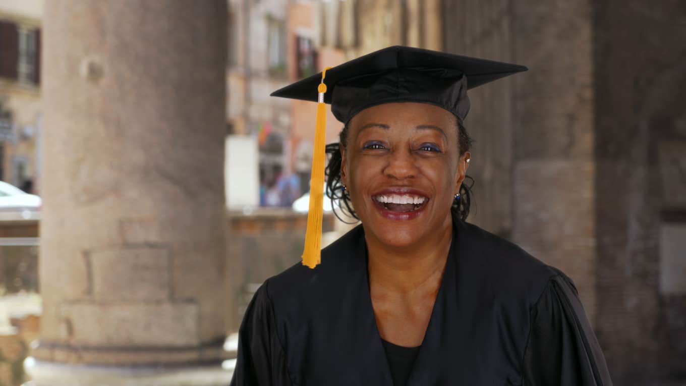 Portrait of senior black woman in graduation gown smiling and cheering