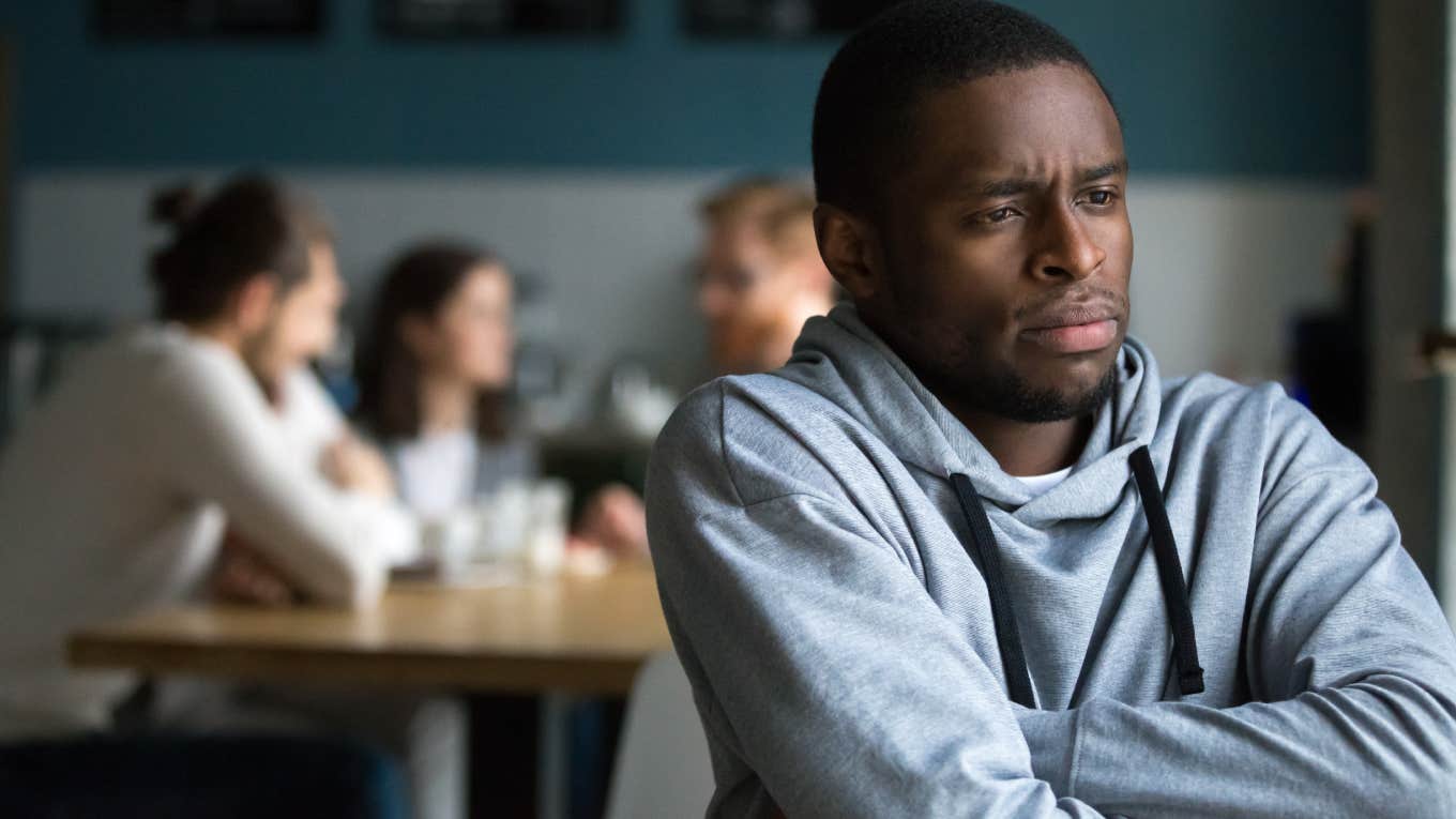 frustrated man sitting alone in cafe from group of people