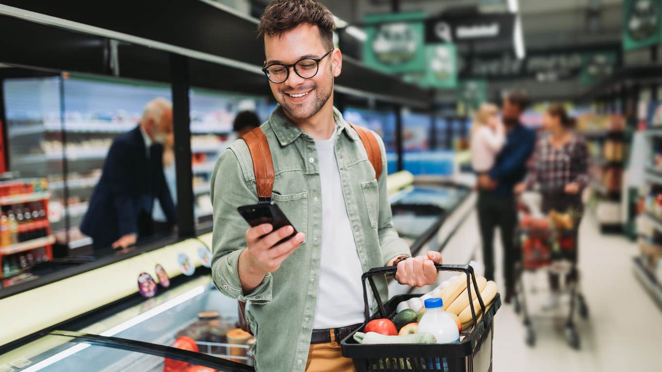 Gen-Z man grocery shopping while on his phone. 