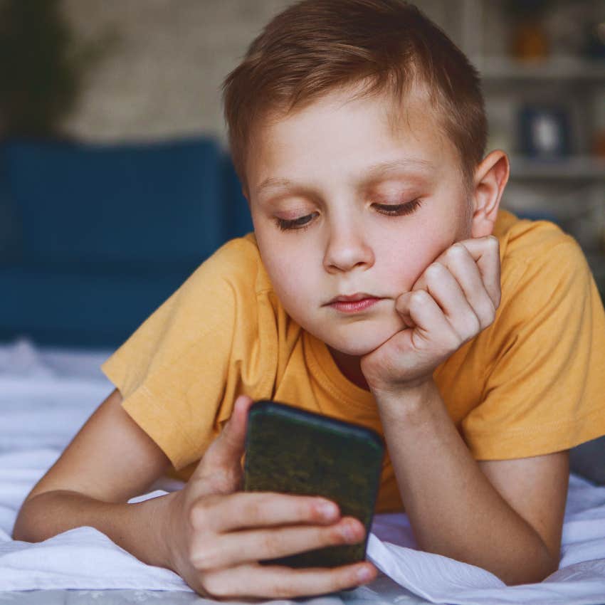 little boy lying on bed looking at phone