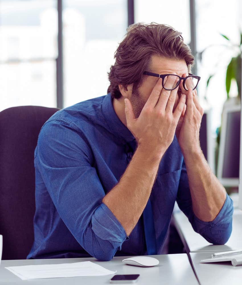 man rubbing his eyes while sitting in front of his computer