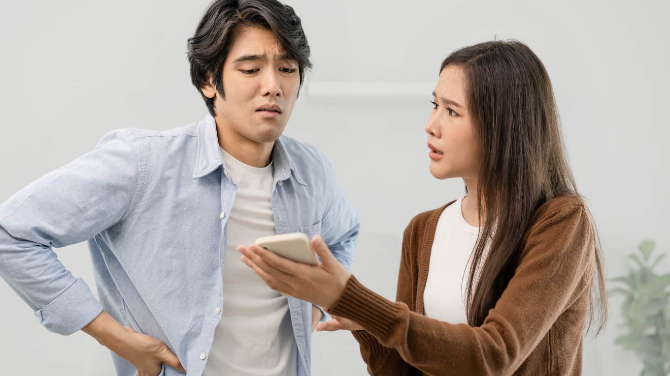 Man looks angrily at girlfriend's phone. 
