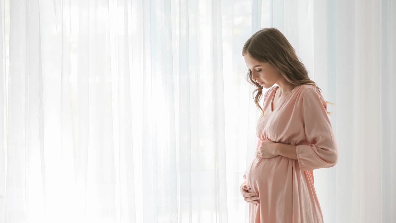 young pregnant woman standing in front of a curtain