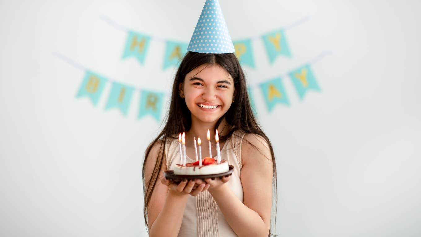 young girl holding cake in front of happy birthday sign