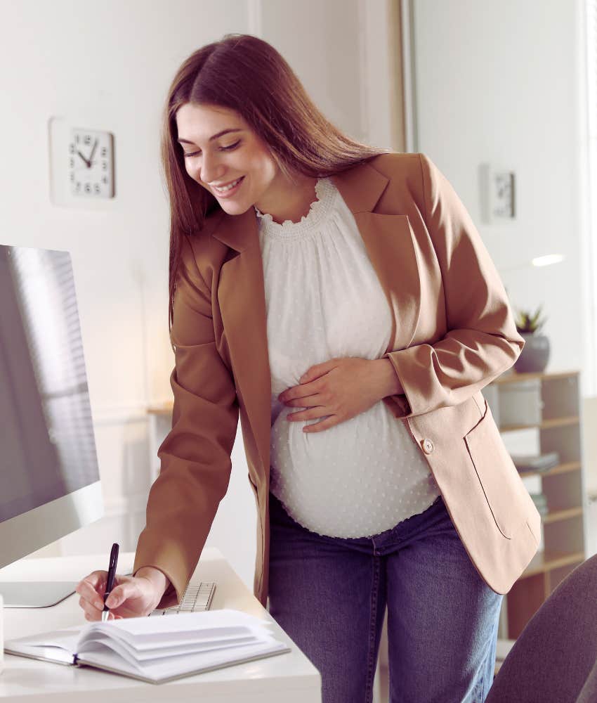 pregnant woman standing in front of desk writing in planner